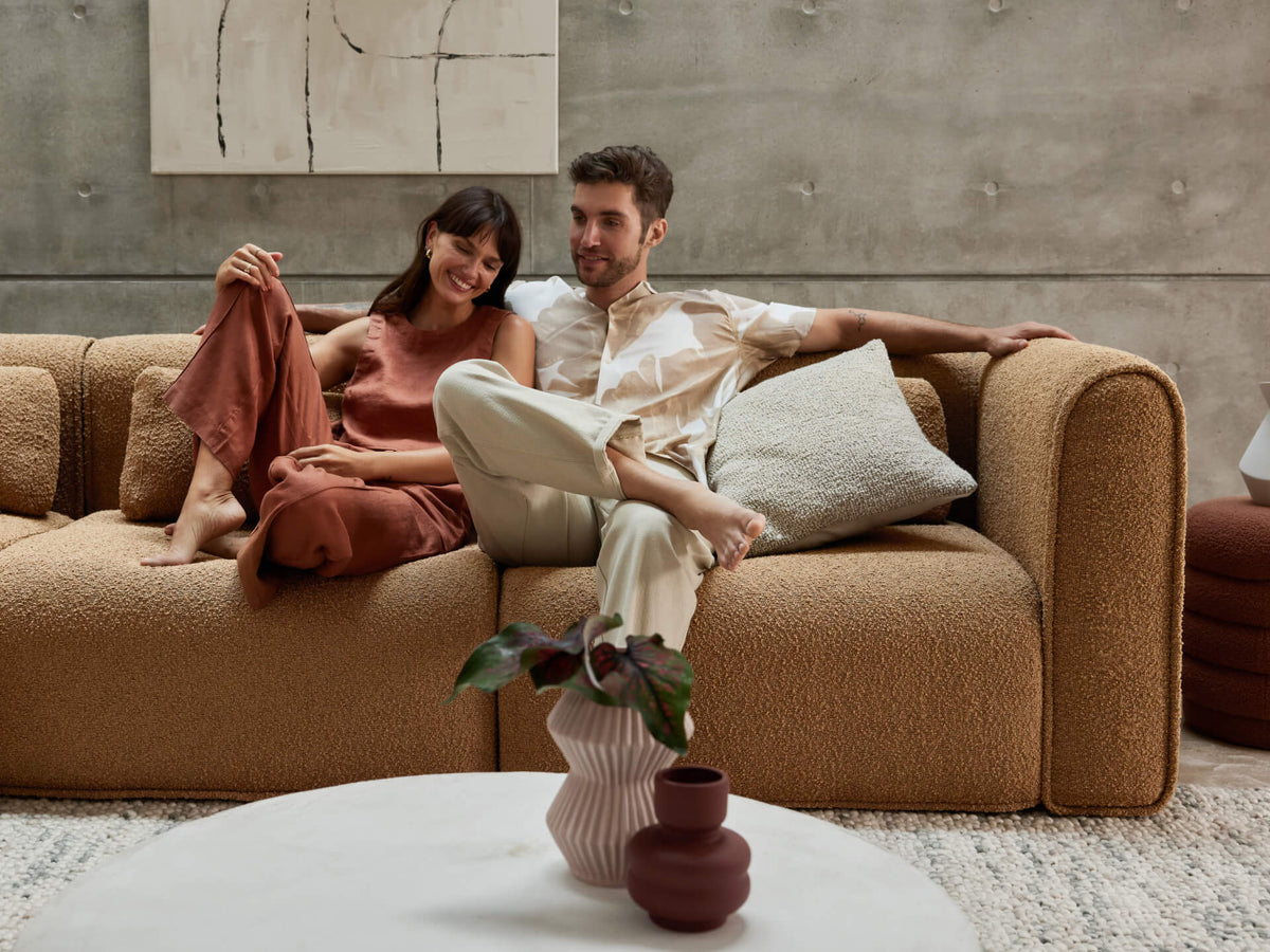 Luxurious boucle sofa in warm beige, featuring plush cushioning and modern block arms. Set in a contemporary living space with concrete walls and abstract art.