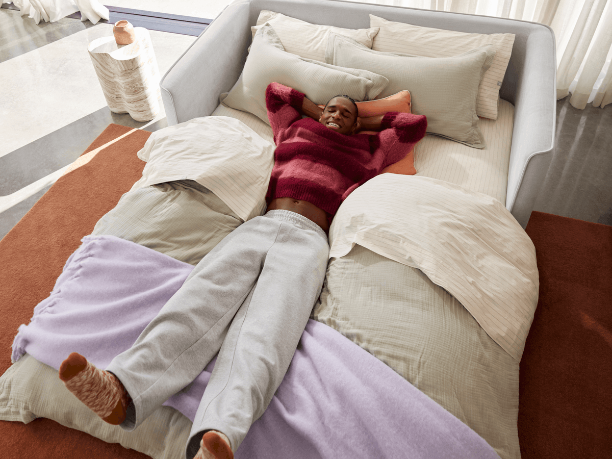 Luxurious grey fabric sofa bed in a modern living space, featuring plush cushions and sleek, minimalist design, accented by layered neutral bedding.